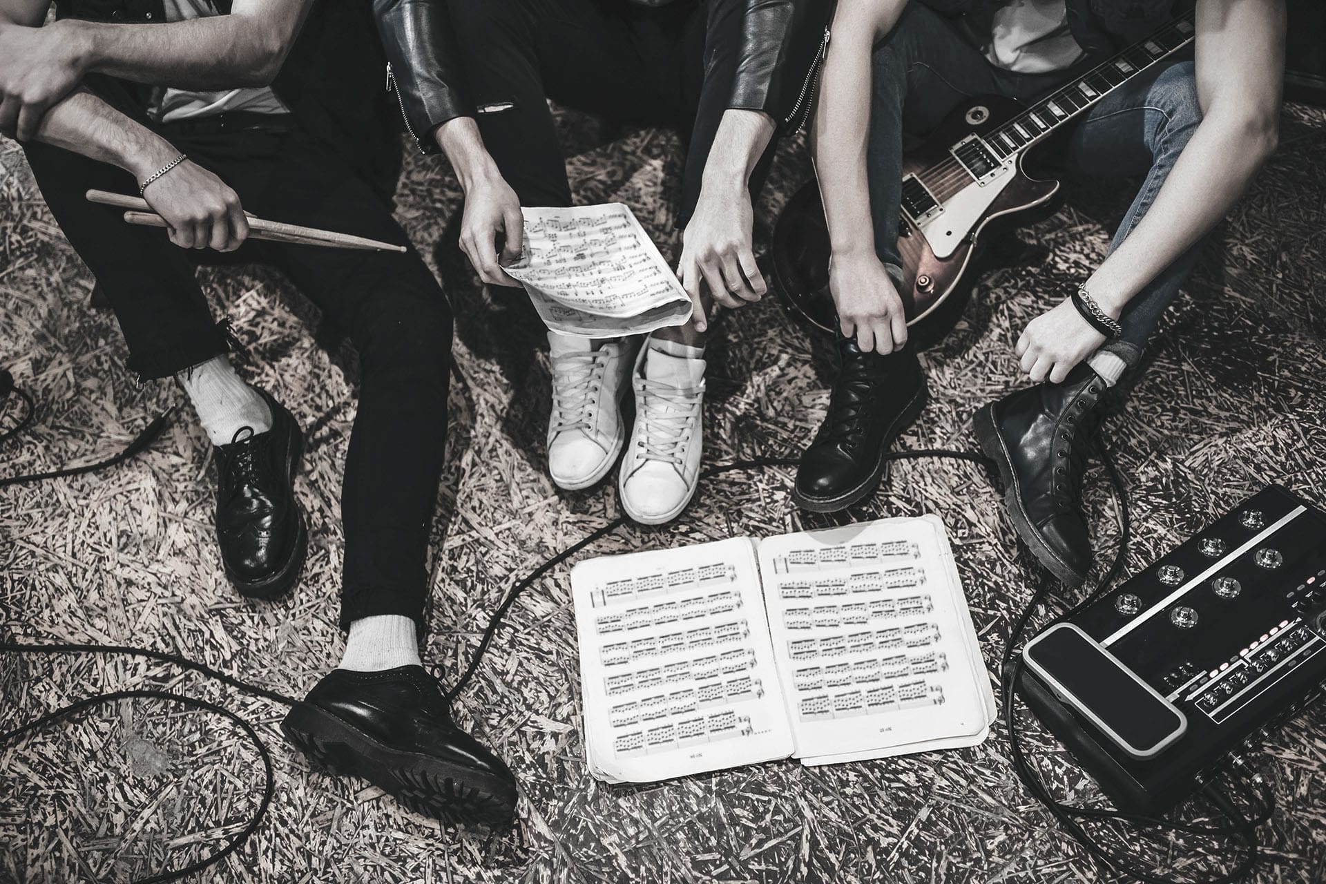 Drei Musiker einer Band sitzen auf dem Boden und gehen Ihre Noten durch.