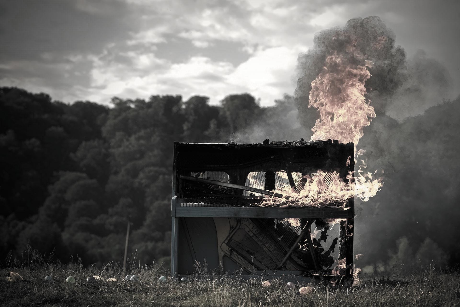 Ein brennendes Klavier auf einem Feld.