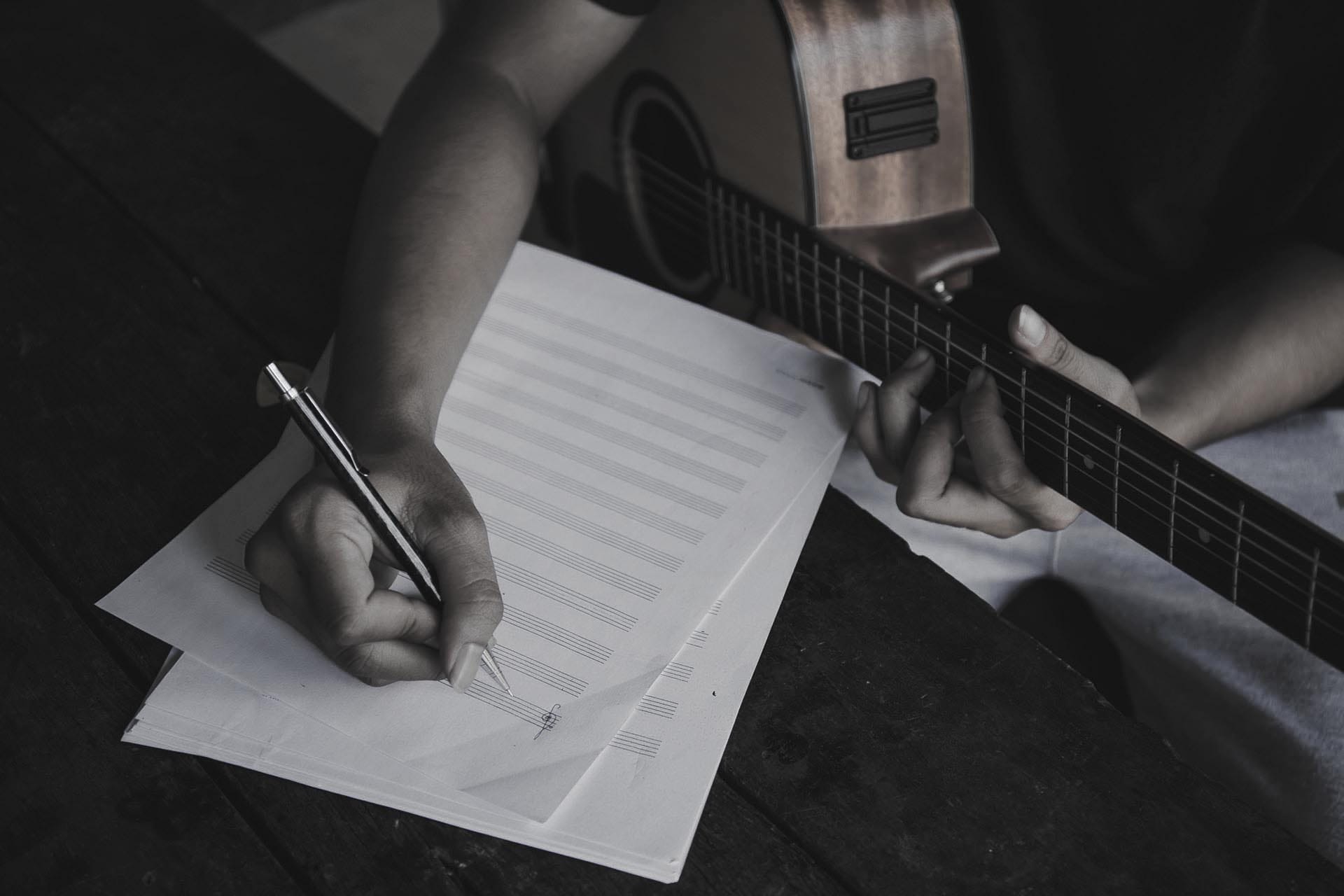 Ein Gitarrist erarbeitet eine Akkordfolge und schreibt sie auf ein Notenblatt.